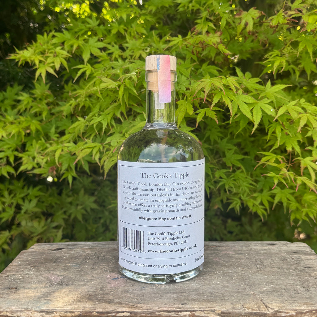 Bottle of 'The Cook's Tipples' gin on a wooden surface with green foliage in the background