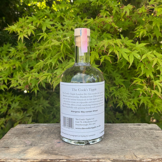 Bottle of 'The Cook's Tipples' gin on a wooden surface with green foliage in the background