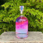 Bottle of 'The Cook's Tipple' gin with a colorful label on a wooden surface with green foliage in the background